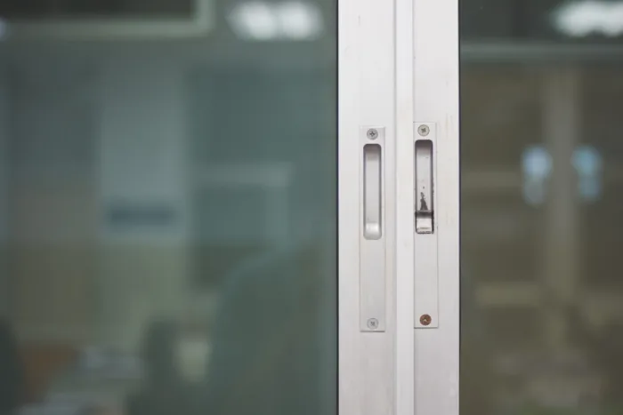 Close-up of a sliding glass door showcasing two vertical metal handles, with a blurred indoor background visible through the glass—perfect for anyone considering a repair or upgrade.