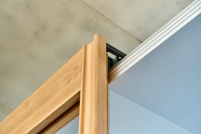 Close-up of a wooden sliding door partially open, revealing the sliding mechanism on a track. Crafted by a local Tampa, FL company, the door's light wood contrasts with the white wall and ceiling in the background.