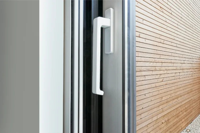 Close-up of a modern white sliding door handle against a glass panel. Next to it, a wall with horizontal wooden siding in Tampa, FL, creates a contrast between the smooth metal and textured wood—a testament to expert craftsmanship beyond mere repair.