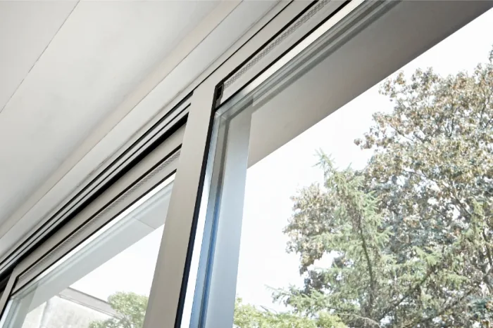 Close-up view of a partially open sliding glass door with a clear view of trees and sky outside. The sleek silver frame not only adds elegance but is easy for local repair services to maintain, allowing natural light to illuminate the minimalist interior space.