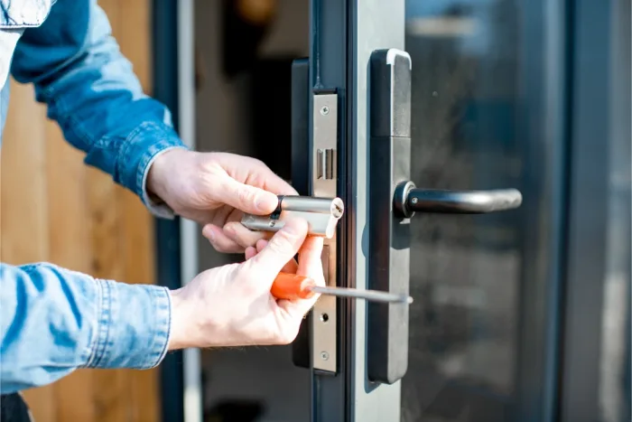 In Tampa FL, a person in a denim shirt expertly repairs the sliding door lock with a screwdriver, focusing intently on their hands and the intricate lock mechanism.