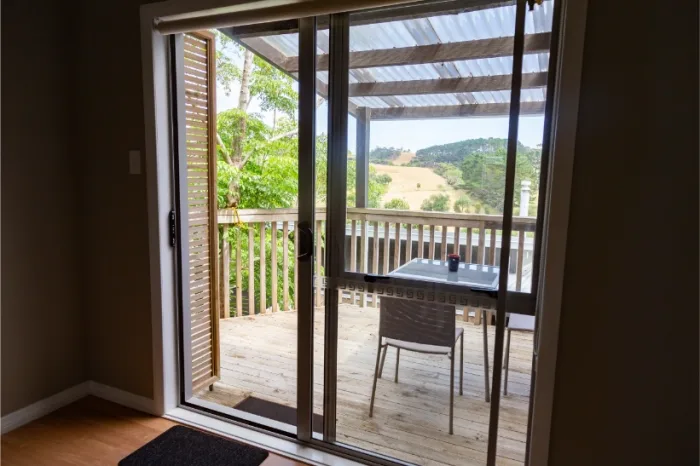 Through the sliding glass doors, a wooden balcony with a single table and chair invites you to enjoy the tranquil rural landscape. The scenic view of green hills and trees under Tampa FL's clear sky offers a perfect escape.