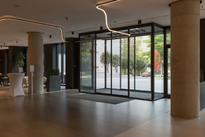 The company's spacious lobby in Tampa, FL, boasts a modern design with large sliding glass entrance doors framed by concrete columns. Inside, minimalist furniture and sleek lighting accentuate the contemporary aesthetic, while greenery peeks through the windows.