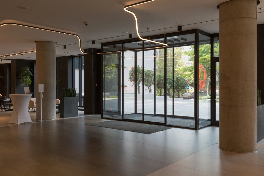 The company's spacious lobby in Tampa, FL, boasts a modern design with large sliding glass entrance doors framed by concrete columns. Inside, minimalist furniture and sleek lighting accentuate the contemporary aesthetic, while greenery peeks through the windows.