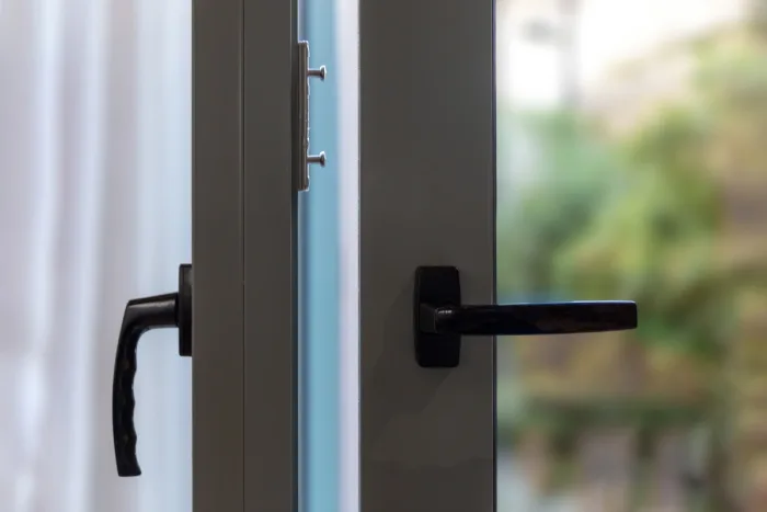 A close-up of a partially open sliding glass door with black handles on both sides. The gray frame contrasts beautifully with the blurred greenery in the background.