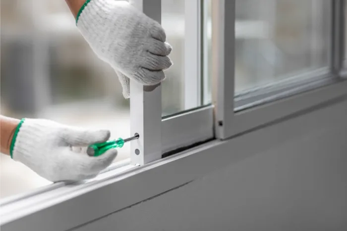 Close-up of a person in Tampa, FL, wearing white gloves as they use a screwdriver to adjust a white sliding window. The scene evokes the meticulous care often associated with maintenance or installation work by a professional company.