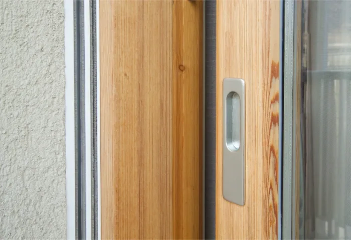 Close-up of a sliding wooden door with a silver handle next to a textured beige wall in Tampa, FL. The door is partially open, revealing a glimpse of a sliding glass panel.